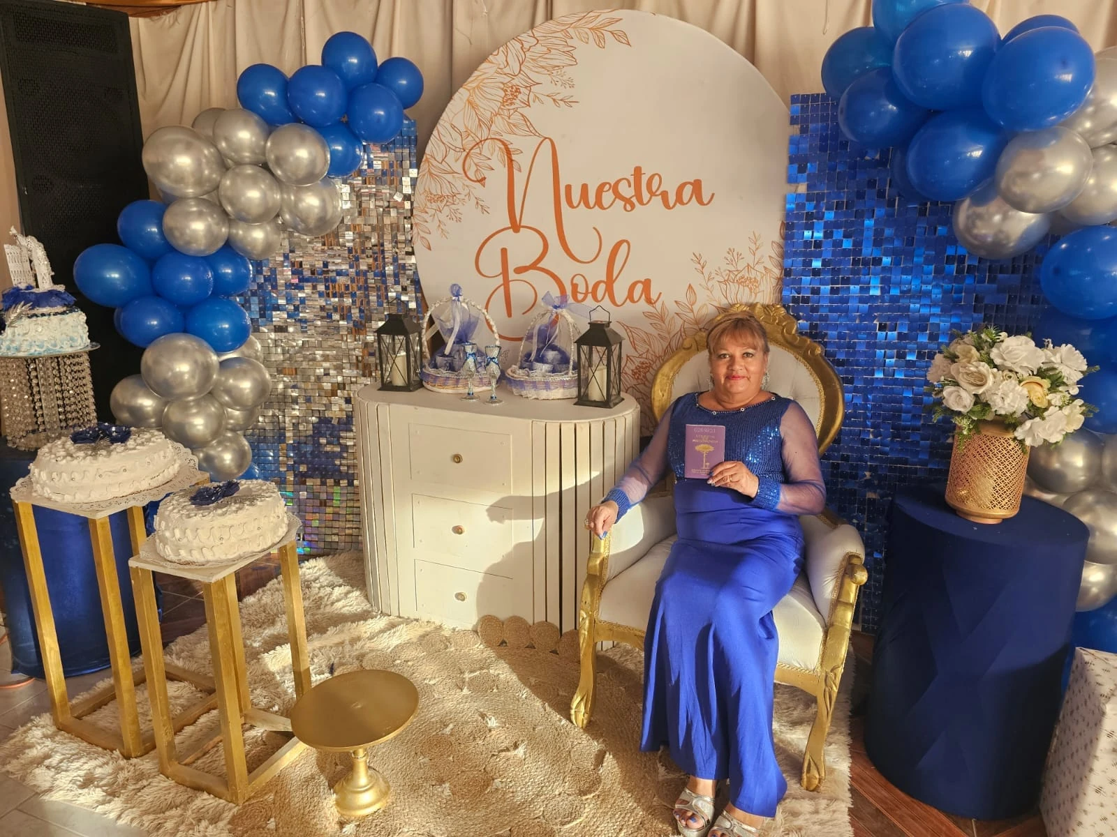 Retrato de una invitada junto a una mesa de celebración y decoración de globos azules y plateados.