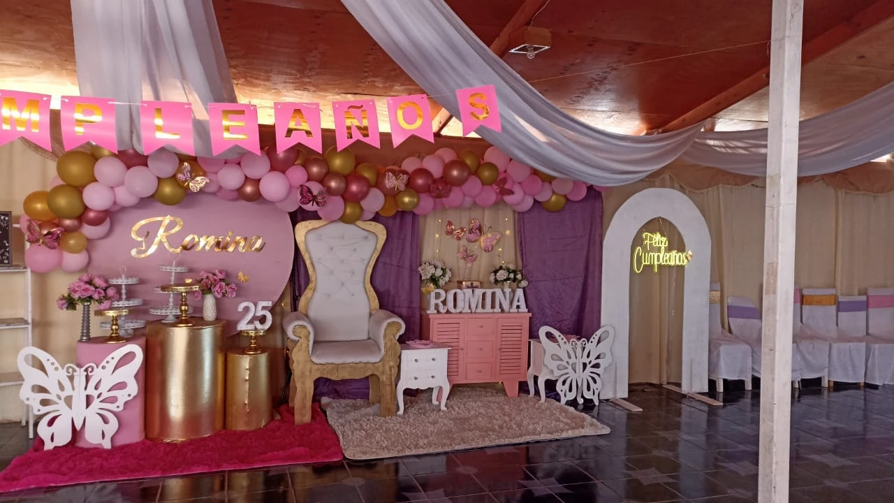 Montaje de cumpleaños en tonos rosados, con globos, flores, mariposas y números decorativos.