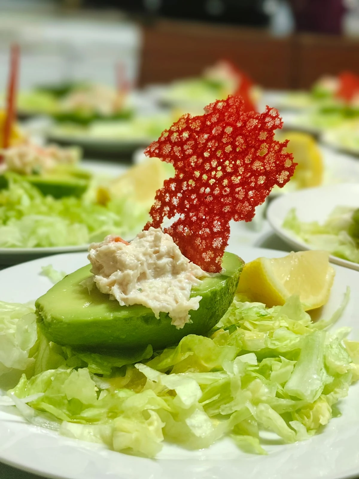 Primer plano de un plato servido sobre hojas verdes, con palta y una decoración crujiente roja.